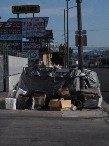 Homeless camp on a urban street corner, boxes, buckets, black tarp.