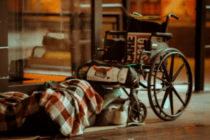 A Wheelchair, with a homless person, covered with a blanket, sleeping beneath it.