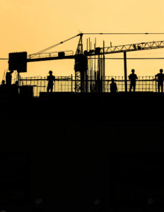 Workers in Silhouette on a rooftop, construction site, crane in the background. Yellow and black.