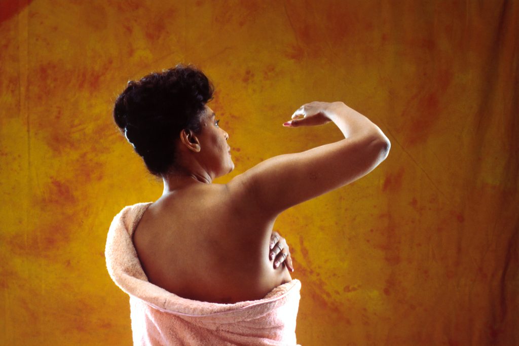 A woman of color conducting a breast self-exam.